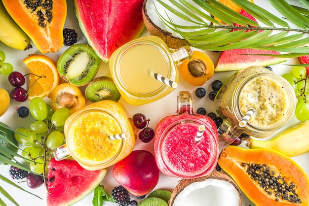 Verschiedene Fruchtsmoothies und -säfte mit tropischen frischen Früchten und Beeren Saubere Ernährung, gesunde Lebensweise, Ernährung und Vitamingetränke-Getränkekonzept Draufsicht flacher weißer Tischhintergrund