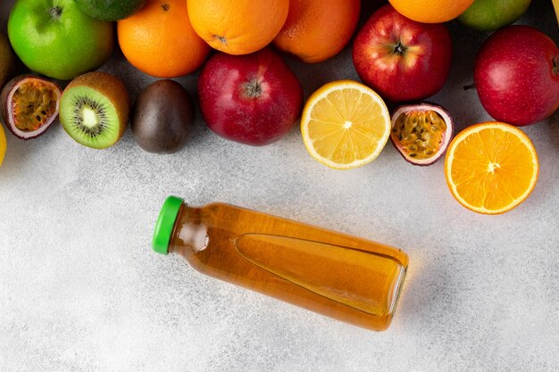 Verschiedene Früchte und frisch gepresster Fruchtsaft in der Flasche auf grauem Hintergrund in Nahaufnahme