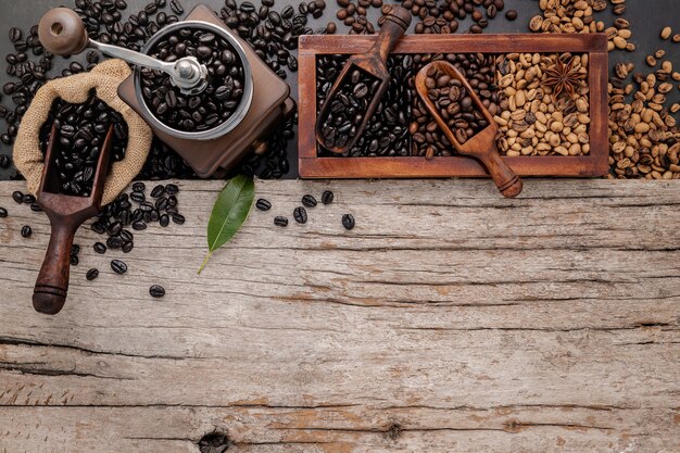 Verschiedene geröstete Kaffeebohnen in Holzkiste mit manueller Kaffeemühle auf schäbigem Holz.