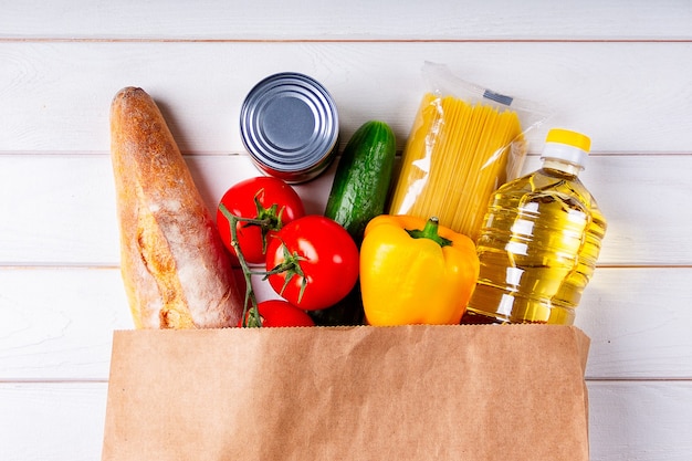 Verschiedene gesunde Lebensmittel, Tomaten, Brot, Nudeln, Gurken, Öl und Pfeffer in Papiertüte auf weißem Hintergrund. Food Delivery-Konzept mit Platz für Text.