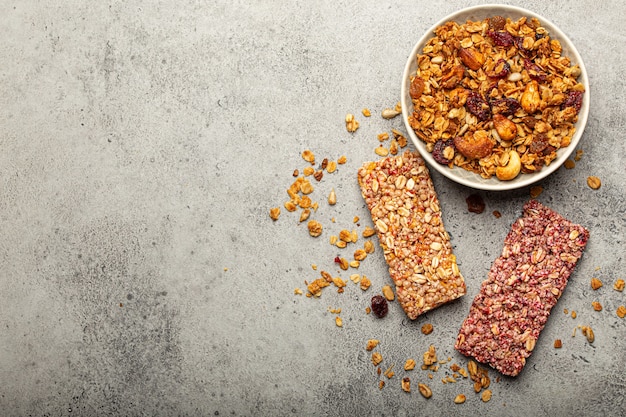 Verschiedene gesunde Müsliriegel mit Nüssen, Samen, Obst und Beeren auf grauem Steinhintergrund, schneller und gesunder Snack oder süße Müsliriegel reich an Energie und Ballaststoffen