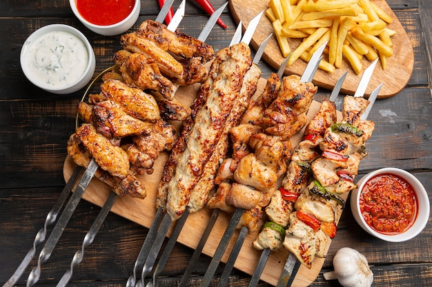 Verschiedene Hähnchenspieße mit Pommes Frites und Sauce auf dunklem Holz