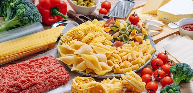 Verschiedene italienische Pastasorten auf Holzhintergrund mit verschiedenen Zutaten zum Kochen traditioneller italienischer Gerichte