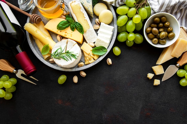 Verschiedene Käsesorten, Trauben, Wein und Snacks auf einem schwarzen Betontisch