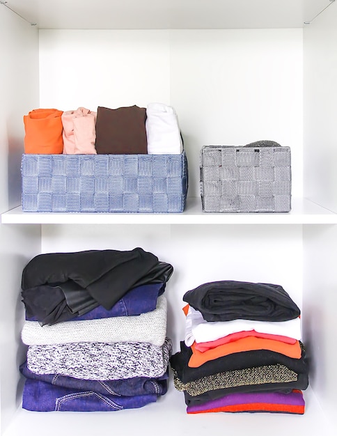 Verschiedene Kleidung in der Hausgarderobe mit Papiernotizen. Kleine Raumorganisation. Vertikale Lagerung. Ausrollhemden in Stoffboxen.