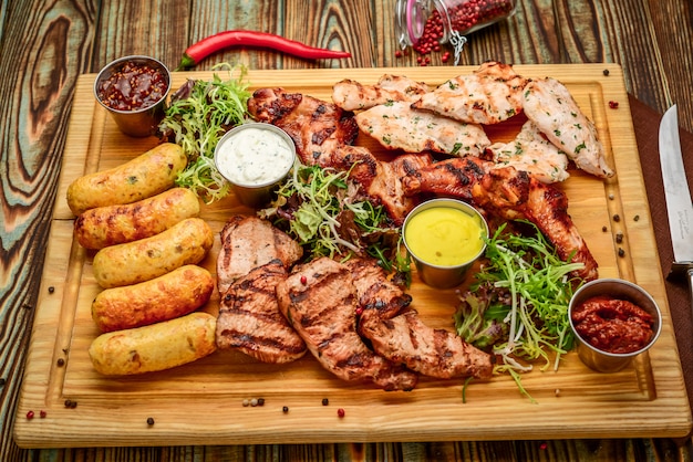 Verschiedene köstliche gegrillte Fleisch- und Gemüsesorten mit frischem Salat und Bbq-Sauce auf Schneidebrett auf Holzhintergrund. Große Auswahl an warmen Fleischgerichten