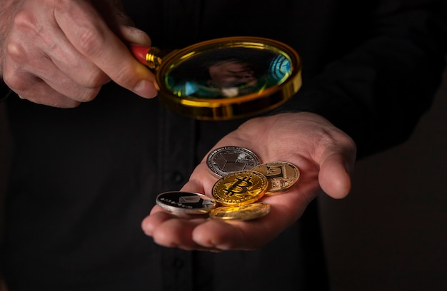 Verschiedene Kryptowährungsmünzen in der Hand mit Lupe Nahaufnahme Haufen von Bitcoin und anderen Kryptowährungen ...