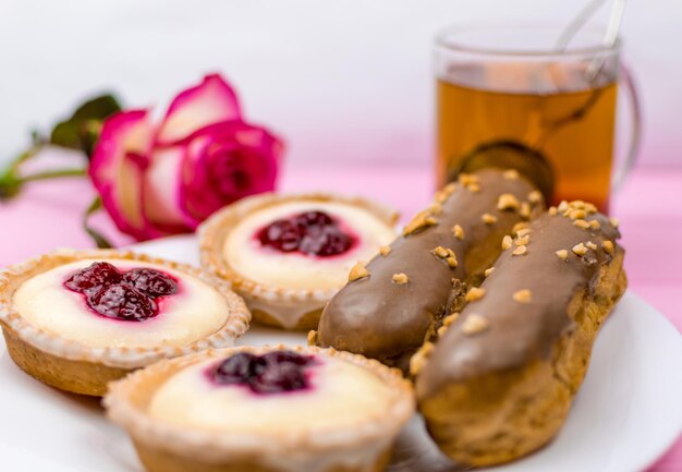 Verschiedene Kuchen mit Pudding und Sahne und Beeren auf einem weißen Teller mit Tee im Hintergrund