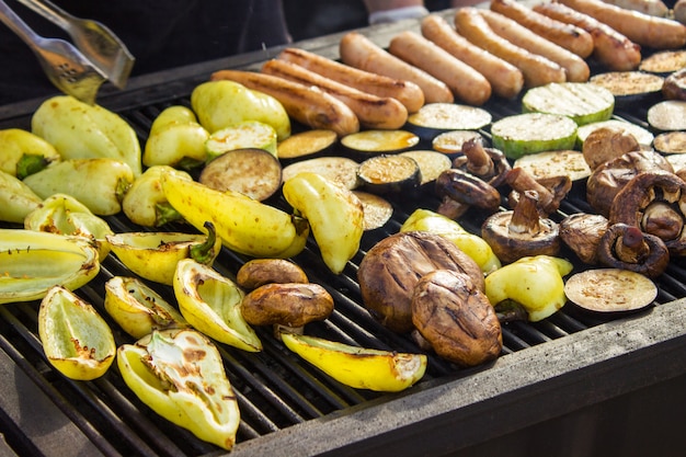 Verschiedene leckere gegrillte Fleischsorten mit Gemüse über dem Grill auf der Holzkohle. Würstchen, Steak, Pfeffer, Champignons, Zucchini.