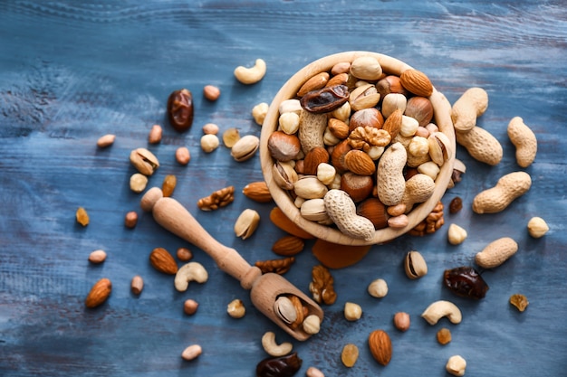 Verschiedene leckere Nüsse mit Schüssel und Schaufel auf Farbfläche