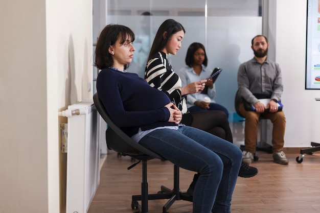 Verschiedene Leute warten im Warteschlangenbüro während des Vorstellungsgesprächs des Unternehmens und halten Rekrutierungsakten bereit, die sich auf das Einstellungstreffen vorbereiten. Multiethnische Gruppe von Kandidaten, die für berufliche Karrieremöglichkeiten rekrutieren