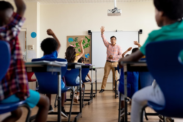 Verschiedene männliche Lehrer und Grundschüler heben in der Klasse die Hände