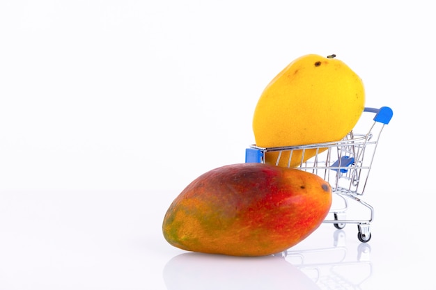 Verschiedene Mangosorten mit gelber, roter Schale in einem Einkaufswagen an einer weißen Wand. Platz kopieren.