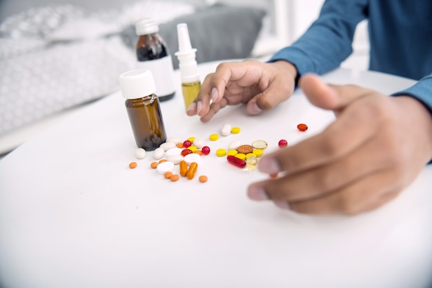 Verschiedene Medikamente. Nahaufnahme von afroamerikanischen Jungenhänden, die sich zu Pillen strecken, die auf weißer Oberfläche liegen