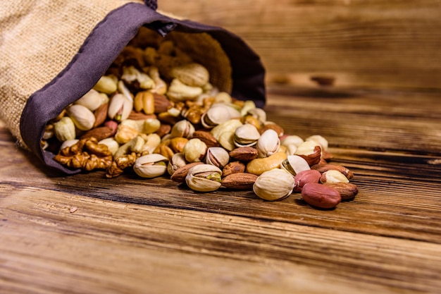 Verschiedene Nüsse Mandel Cashew Haselnuss Pistazie Walnuss verstreut aus Beutel auf einem Holztisch Vegetarische Mahlzeit Konzept für gesunde Ernährung