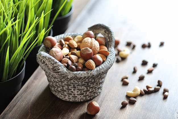 Verschiedene nützliche und leckere Nüsse auf einem Holztisch und Töpfe mit grünem Gras