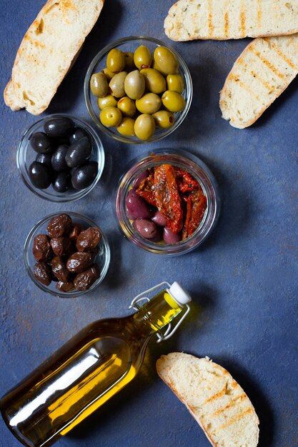 Verschiedene Olivensorten, Bruschetta, getrocknete Tomaten und Olivenöl. Mediterrane Snacks. Ansicht von oben.