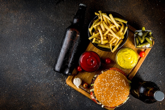 Verschiedene Partygerichte, Hamburger, Pommes, Kartoffelchips, eingelegte Gurken, Zwiebeln, Tomaten und kalte Bierflaschen