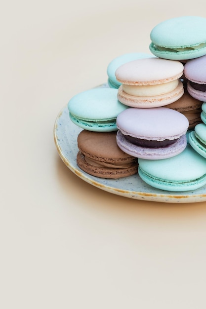 Verschiedene pastellfarbene Gebäck-Macarons auf einem Teller auf einem beigen vertikalen Hintergrund