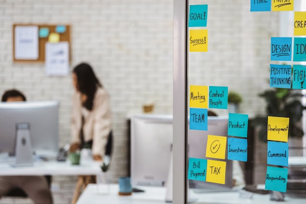 Verschiedene Post-It-Notizen mit Geschäftsstrategie-Wortlauten über der Glaswand im Büro