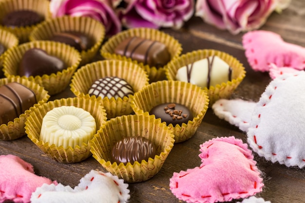 Verschiedene Pralinen mit rosa Rosen auf Holztisch.