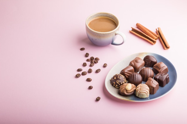 Verschiedene Pralinen und eine Tasse Kaffee auf einem rosa Pastellhintergrund. Seitenansicht, Kopierraum.