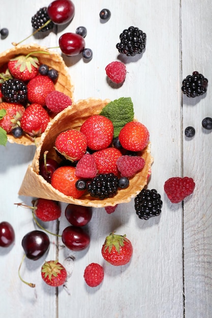 Verschiedene reife Beeren in Zuckerkegeln auf weißem Holzhintergrund