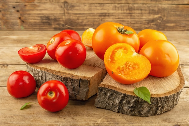 Verschiedene reife Tomaten auf einem Holzständer. Frisches rotes und oranges Bio-Gemüse, Basilikumblätter. Alter Holztisch, Nahaufnahme