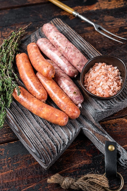 Verschiedene rohe schweine- und rindfleischwürste mit gewürzen auf einem holzbrett mit thymian. dunkler hölzerner hintergrund. ansicht von oben.