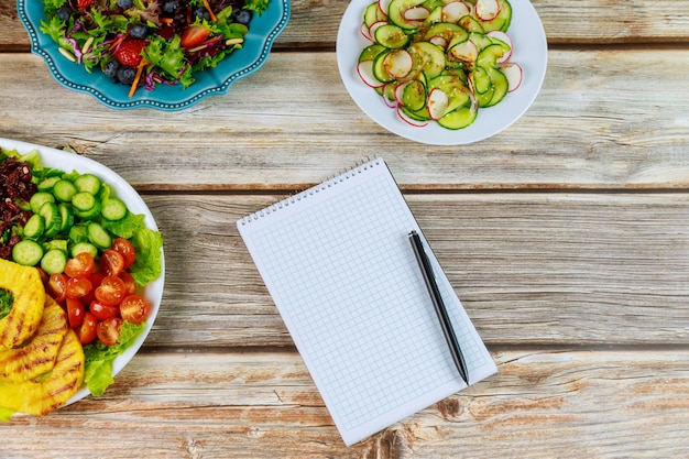 Verschiedene Salate mit Notizbuch und Stift auf Holztisch