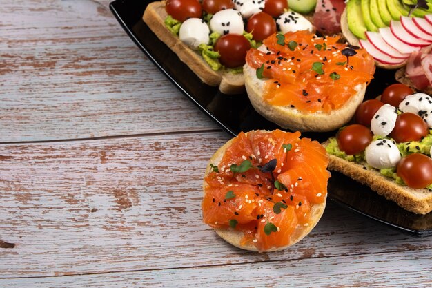 Verschiedene Sandwiches mit Fisch, Käse, Fleisch und Gemüse auf einem schwarzen Teller