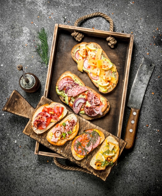 Verschiedene Sandwiches mit Meeresfrüchten, Fleisch und Gemüse auf einem alten Tablett. Auf einem rustikalen Tisch.