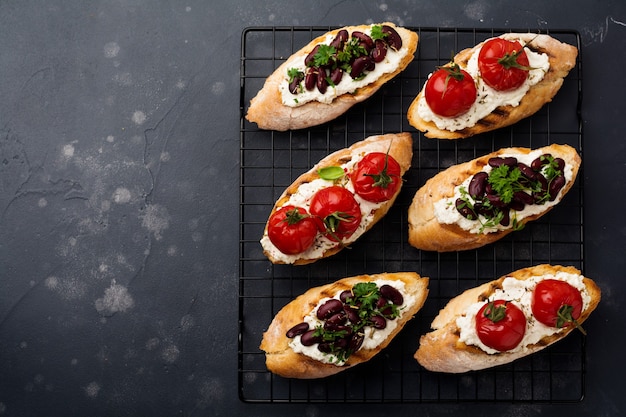 Verschiedene Sandwiches mit roten Bohnen, gebackenen Kirschtomaten, Knoblauch, Olivenöl und Quark auf dunkler Oberfläche