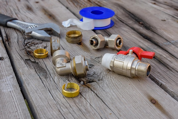 Verschiedene Sanitär-Ersatzteile, Dichtband und verstellbarer Schraubenschlüssel auf Holzuntergrund