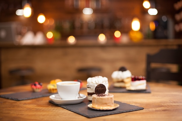 Verschiedene Scheiben köstlicher Kuchen auf einem Holztisch in einem Café. Stück leckerer Kuchen mit Keks obenauf. Köstliche Tasse Kaffee.