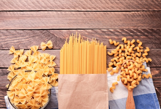 Verschiedene Spaghetti-Nudeln, Schmetterlinge, Locken auf hölzernem Hintergrund Nahaufnahme. Der Blick von oben