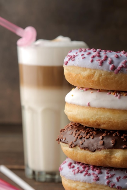 Verschiedene süße Donuts mit Zuckerguss und Toppings und Kaffee Latte auf einem braunen Holztisch