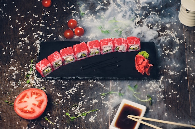 Verschiedene Sushi auf weißem Teller mit Stäbchen auf hölzernem Hintergrund.