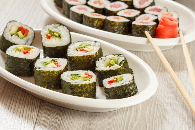 Verschiedene Sushi-Rollen mit Reis- und Algenblättern auf Keramikplatten, Essstäbchen und eingelegtem Ingwer. Ansicht von oben.