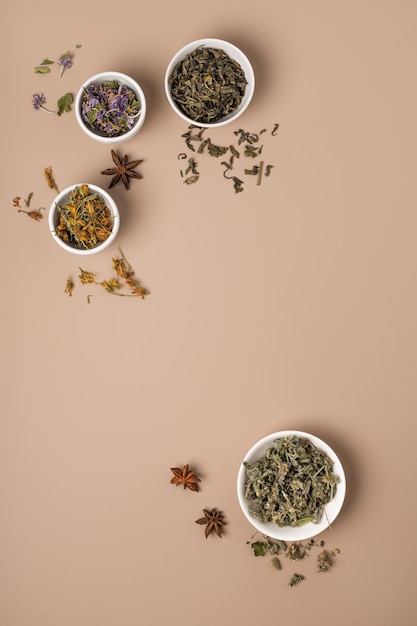 Verschiedene Teesorten und Kräuter in Schalen auf beigem Hintergrund