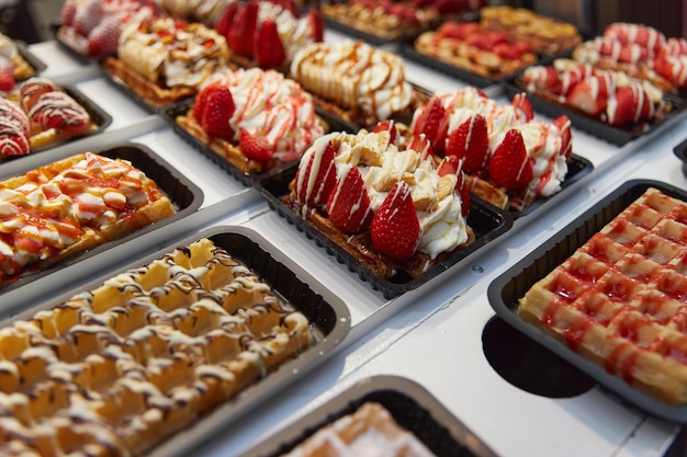 Verschiedene traditionelle belgische Waffeln mit Schokoladen-Spekulatius-Schlagsahne und Obst in einer Ladenfront in Brüssel