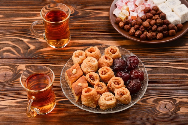 Verschiedene traditionelle östliche Desserts mit Tee auf Holzhintergrund Arabische Süßigkeiten auf Holztisch Baklava Halva Rahat Lokum Sherbet Nüsse Datteln Kadayif auf Platten Platz für Text