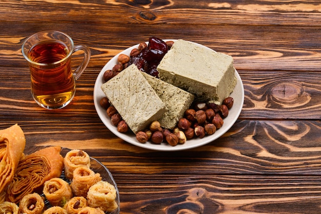 Verschiedene traditionelle östliche Desserts mit Tee auf Holzhintergrund Arabische Süßigkeiten auf Holztisch Baklava Halva Rahat Lokum Sherbet Nüsse Datteln Kadayif auf Platten Platz für Text