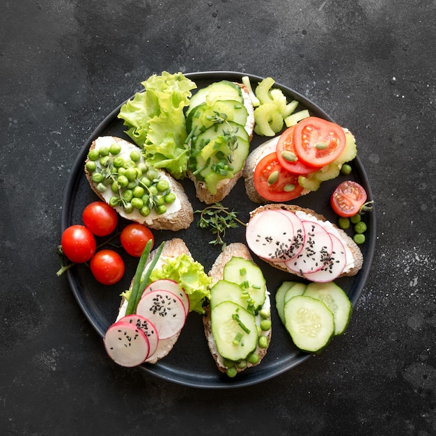 Verschiedene vegane Sandwiches mit Gemüse, Rettich, Tomate, Roggenbrot auf Schwarz. Vorspeise für Party.