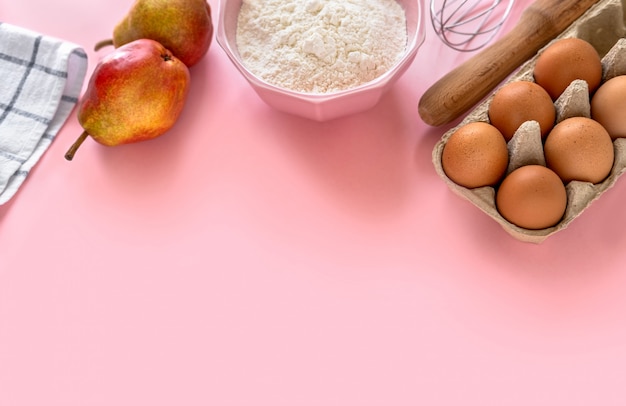 Verschiedene Zutaten zum Backen auf einem rosa Hintergrund flach gelegt.