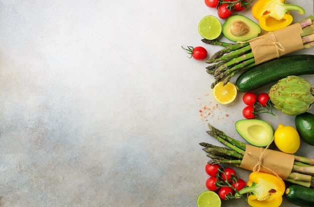 Verschiedenes organisches Gemüse - Spargel, Tomatenkirsche, Avocado, Artischocke, Pfeffer, Kalk, Zitrone, Salz auf grauem Hintergrund.