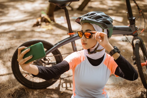 Verschleiertes Mädchen mit Sonnenbrille Selfie mit Smartphone beim Radfahren