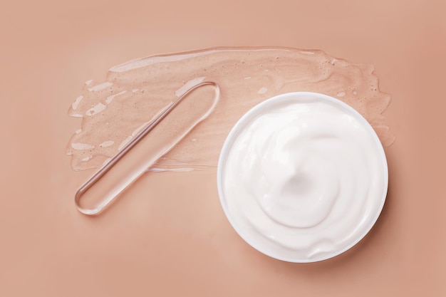 Verschmiertes transparentes Gel auf dem Hintergrund. Spatel zum Auftragen der Creme. Ein rundes Glas kosmetischer weißer Creme auf beigem Hintergrund