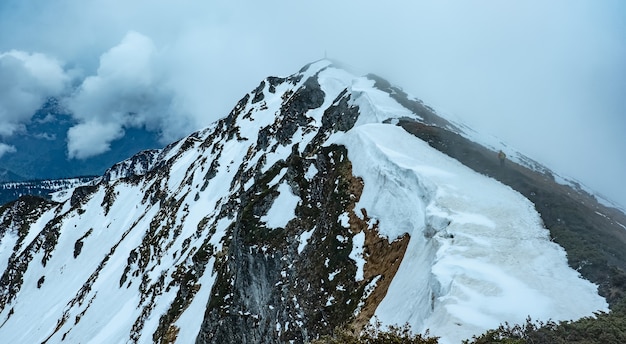 Verschneite Berglandschaft, teilweise nebelverhangen, mit einsamen Wandertouristen, die auf dem Hügel stehen