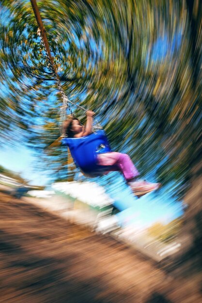 Verschwommene Bewegungen eines Mädchens, das im Park auf einer Schaukel schwingt